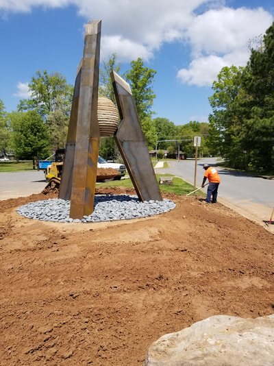 4/23/17: We're pleased to announce that NSG's Stephen Shachtman won this year's Sculpture at the River Market public art competition. Stay tuned to see it actualized and installed at the Southwest Community Center. This sculpture represents a culmination of parts forming a stronger, more impactful unit as a result. The graphic nature of the sculpture is ideal for both ease of viewing while in motion and creating an iconic sculpture for the Community Center campus. Because this site incorporates so many activities and houses several public buildings, the convergence of this is represented in this form - a central piece acts as the hub of all the opportunities the campus offers. At the heart of the three steel forms is a sphere representing the community. The Steel/Bronze portion of the “A” represents Arkansas. While the individual pieces of the flagstone sphere make up my notion its people. Fabricated in CorTen steel, with a Bronze cap at the point of each pillar. The tallest form measures approximately 16-feet high. The overall footprint will span approximately 10ft wide. The center sphere is composed of stacked flagstone pieces which create the stepped sphere form. (Not a perfect smooth sphere, but stepped to create sphere appearance.) The sphere structurally helps connect the three legs, which are then bolted into cement piers. I recommend contextualizing the artwork within the broader site by placing it in a large gravel circle of grey breeze, and planting karl foerster grasses within.