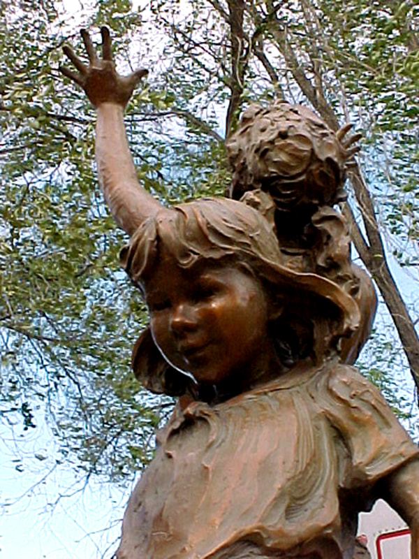 Touch the Sky by Fellow Jane DeDecker and the National Sculptors' Guild was placed through a public art call at 525 E. Bridge Street, Brighton, Colorado.

This bronze sculpture of four children playing on and around a large tree stump was created in 1997. It was conceived to meet the need of a sculpture with children that had enough o fa presence to be placed in a large park and not seem dwarfed by the surroundings. The artist effectively solved this problem by using a large tree stump as a prop. This prop gives the sculpture enough mass to hold its own in the great outdoors. The children on the stump represent a number of emotions that all children have. The girl with hands raised to the sky exudes the exhilaration of the moment. One of the children on the log shows the tentativeness of being on top of the stump. A little boy at the base of the stump is in his own world looking at a bug. In all, the work carries the theme of the circle of life and the many experiences that go with it: from the fallen tree to the children’s exploration of life. The monument is 8’9”H 5’W and5’D. It has been placed at ground level so that children may easily relate to it. Decorative grasses will surround it giving it a naturalized appearance that is appealing year-round.

​NSG Public Art Placement #138