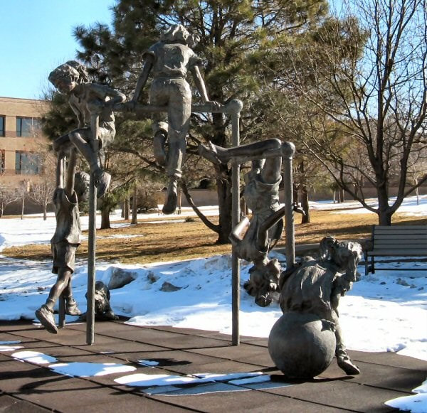 The National Sculptors' Guild placed Fellow Jane DeDecker's "Jungle Gym" in Westminster, Colorado in 1995. The 125% life-size multi-figurative bronze features five-children at play on a jungle gym, joined in by a dog tugging at the laces of one of the kids. The piece is a reminder of simpler days of play in parks and schools. 

The sculpture measures 11ft tall, 15ft wide, 5ft deep.

NSG public art placement 9